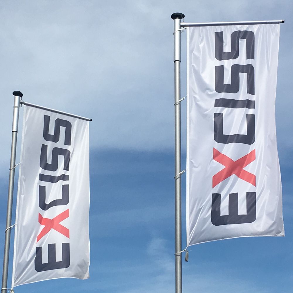 Two company flags with the EXCISS logo against a blue sky
